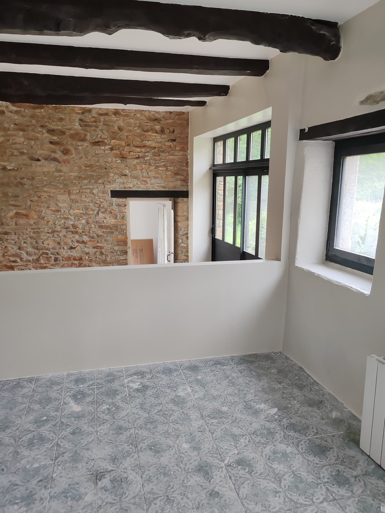 Salle rénovée avec mur pierre, verrière et carrelage motif ciment